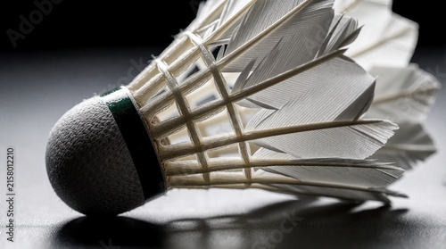 Shuttlecock detailed close-up side view on dark grey surface. Badminton birdy with white feathers and grey cork base. Sports equipment for game or competition.