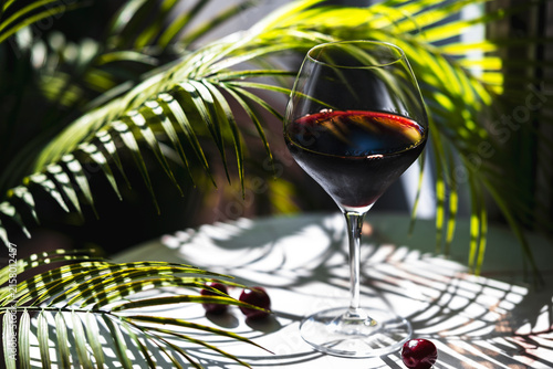 Quadro su tela Chilean Carmenere red wine glass with sweet cherries among bright green palm fro