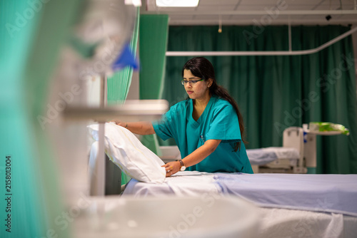 Sticker Healthcare worker in scrubs arranging a hospital bed in a ward.