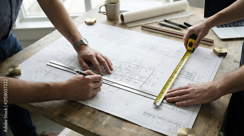 Two people collaborating on architectural plans at a wooden table