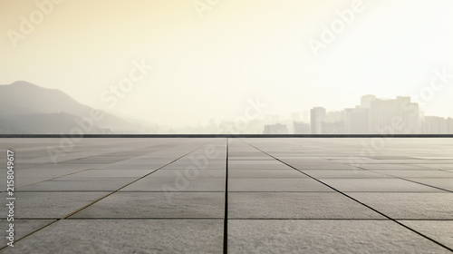 Empty gray tiled terrace floor extends into the distance with misty mountains and city outlines in the background.