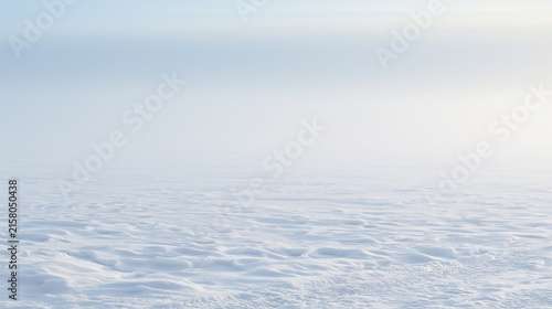 Vast white snowy field extending to the horizon forming a minimalist composition with pale blue sky.