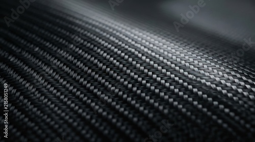 A close-up shot of carbon fiber material. The dark, textured surface displays a prominent woven pattern.