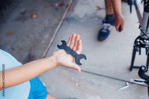 Fotografía Close-up of a child's hand holding a black metal wrench outdoors during a family bicycle assembly and maintenance session