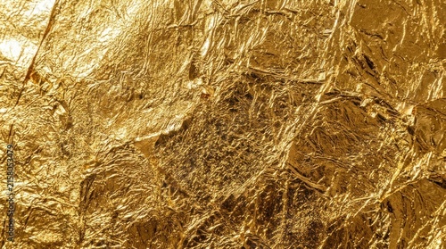 A close-up shot of shimmering gold leaf, creating a textured and reflective surface. The gold appears to be crumpled and layered, with intricate patterns and highlights.