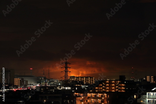 光害：フレアスタックの炎が照らす雲と都市の夜景 / Light pollution: Flare stack flames illuminating clouds over a city at night