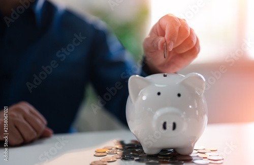 Close-up Hand putting coins into a white piggy bank saving bank for account save money. Planning step up, saving money for future plan, retirement fund. Business investment-finance accounting concept.