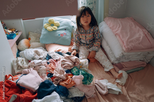 Child Sitting in Messy Room With Clothes Scattered Around