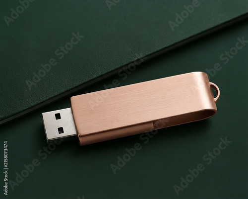 Metal USB drive resting on a dark green surface next to a notebook