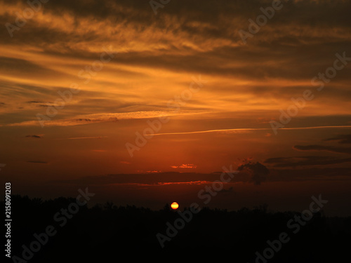 Cuadro en lienzo Dramatic orange sunset sky with sun dipping below dark horizon