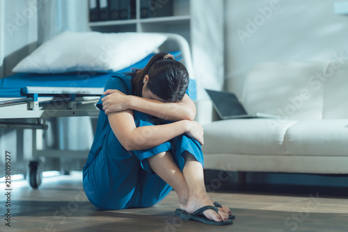 Konstfotografi Distress in Scrubs: A healthcare worker, overcome with emotion, sits on the floor of a room, hugging her knees in a moment of deep despair