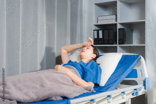 Canvas Print Sick Patient in Hospital Bed: A young patient lies in a hospital bed, looking unwell with a feverish forehead and closed eyes, conveying a sense of vulnerability and illness