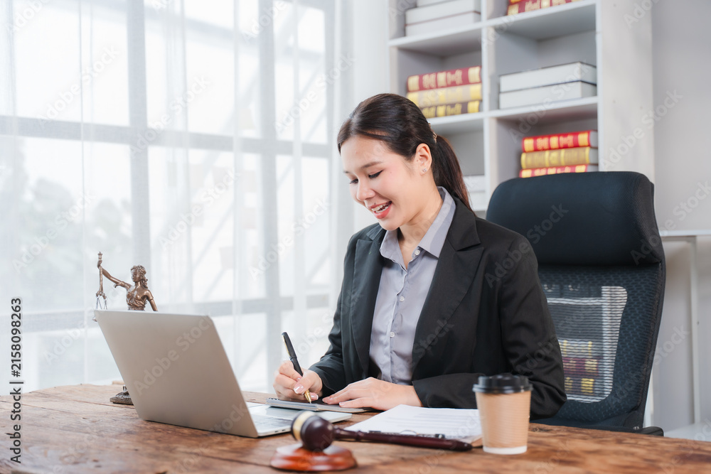 Fototapeta premium Legal Professional at Work: A focused female lawyer, poised and professional in her office, reviews documents on her laptop while taking notes, symbolizing dedication to justice and legal practice.