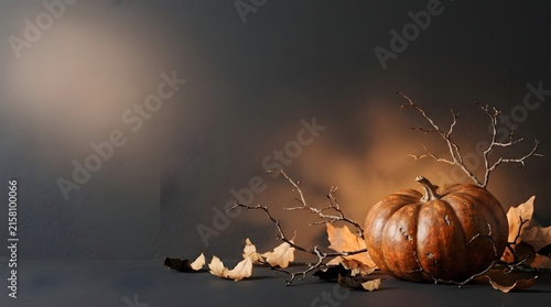 A rustic autumn composition featuring a single orange pumpkin surrounded by dried fall leaves and warm candlelight