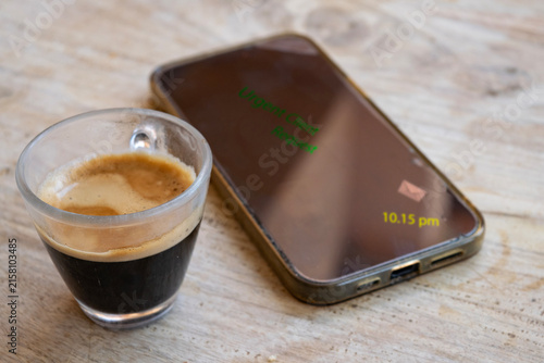Espresso coffee cup next to modern smartphone showing urgent notification on wooden table background