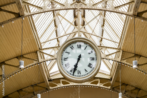 фотографія Large vintage clock hanging beneath an ornate glass and iron station roof