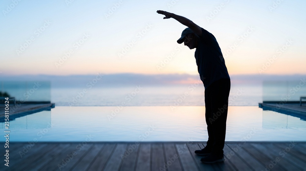 Fototapeta premium Silhouette of Senior Man Performing a Side Stretch at Sunset