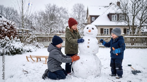 Three children building a snowman in a snowy backyard, wearing winter jackets, hats, and gloves, with a wooden sled and house in the background