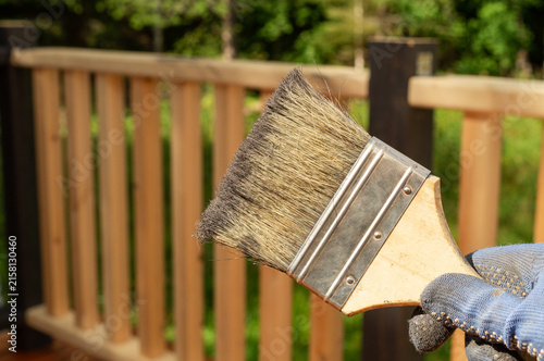 Foto Hand in protective glove painting a wooden deck railing with a brush outdoors
