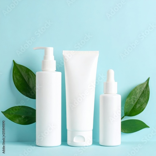 three white plastic bottles with green leaves on blue background