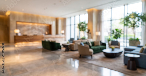 A blurred view of a modern hotel lobby featuring stylish furnishings, plants, and a reception area, creating a welcoming atmosphere for guests.