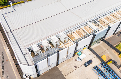 Aerial drone image of a modern data centre roof, with existing industrial cooling HVAC units alongside pre-built empty framework for expansion