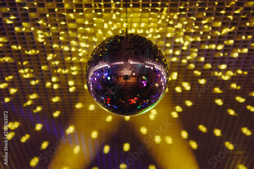disco ball with mirror surface and bright rays, yellow purple light, hanging on ceiling, night party background