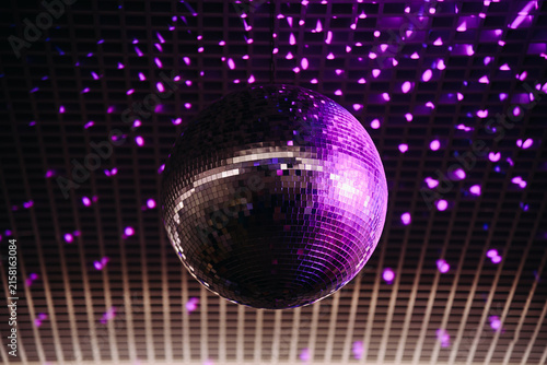 disco ball with mirror surface and bright rays, purple light, hanging on ceiling, night party background