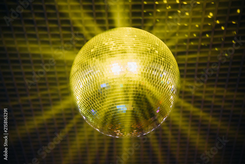 disco ball with mirror surface and bright rays, yellow light, hanging on ceiling, night party background