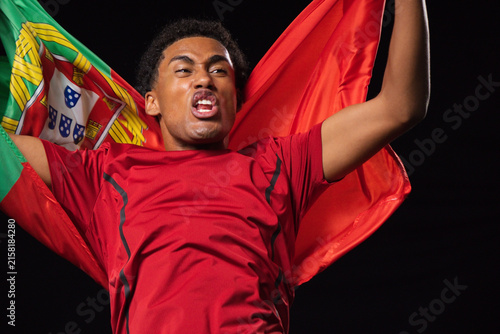 Man shouting and celebrating while wearing red athletic shirt with Portuguese flag at stadium