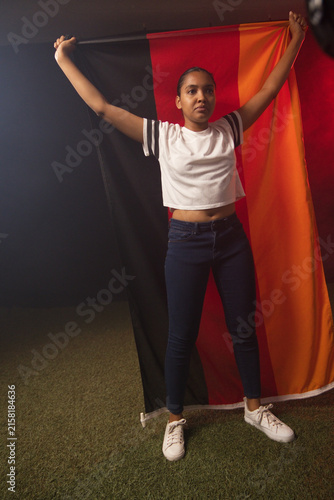 African American woman holding black red orange flag overhead in studio on turf wearing white shoes