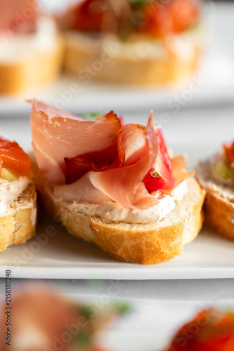 Foto A close-up shot of elegant crostini appetizers topped with whipped cream cheese, ribbons of prosciutto, and fresh tomatoes served on a white platter