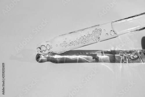 Glass pipette with facial serum on a light background. Essential oil close-up in a pipette. A skin care product with hyaluronic acid in a pipette.
