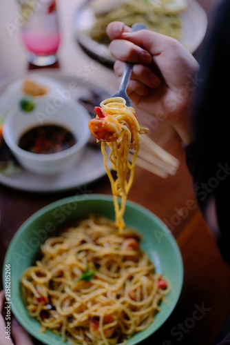 Person eating delicious spaghetti pasta with a fork from a green bowl at a restaurant