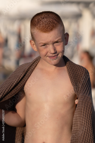 Adorable boy wrapped in towel after swimming at tropical beach. Teenage boy on a public beach wrapped in a towel. Peaceful tropical summer holiday, travel, relaxation, summer vacation,