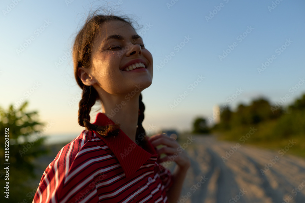 Naklejka premium A happy young woman with braids enjoying sunset outdoors. Lifestyle portrait of a smiling female expresses freedom, joy, and peace in a natural summer environment.