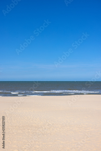 Pristine wide sandy beach under a clear blue sky stretching toward gentle ocean waves in Middelkerke - Belgium