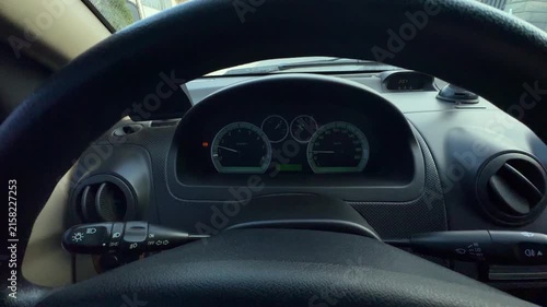 Driver seat cockpit view showing steering wheel rim, inactive instrument cluster, hood vents, stalk controls, dashboard trim, gauges, dials, glass reflections, dark interior