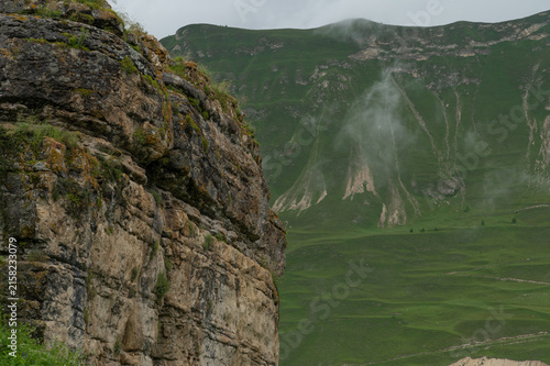 Rolling green slopes rise beneath heavy clouds and soft mist