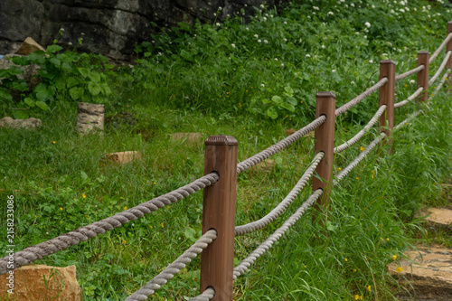 Rope fence with wooden posts borders green meadow gently
