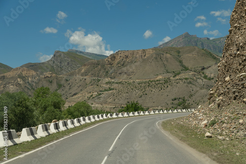 Winding mountain road curves through rugged hills under blue sky