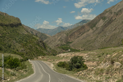 Winding mountain road curves through rugged hills under blue sky