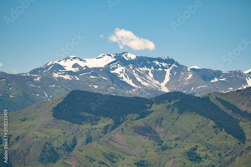 Majestic snow-capped mountains rise above rolling green hills