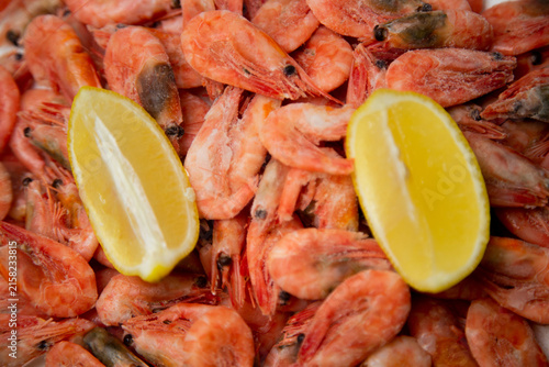 A close-up of a filled frame with tightly lying frozen pink shrimp and two bright lemon slices creating a contrast. Concept: filling the space with seafood texture. High quality photo