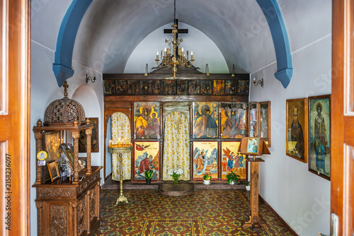 Konstfotografi A small Greek Orthodox chapel featuring a wooden iconostasis, patterned tile flooring, and a vaulted ceiling with blue structural arches in the village of Agios Nikolaos, Greece, island of Crete