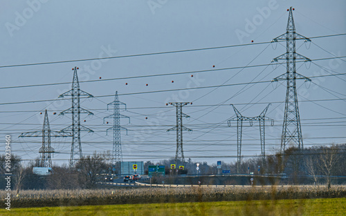 Obraz na plátně Dense network of high-voltage transmission lines and electricity pylons beside a road junction and agricultural landscape, illustrating modern power and transport infrastructure