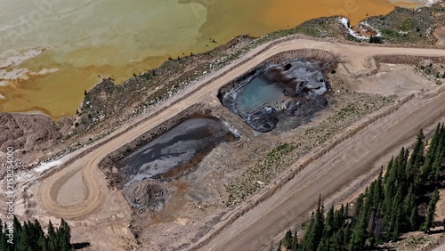 Aerial view of Mayflower Tailings Pond showing industrial mining ponds with discolored water, surrounding dirt roads, and pine forest edges in Summit County, Colorado, United States.