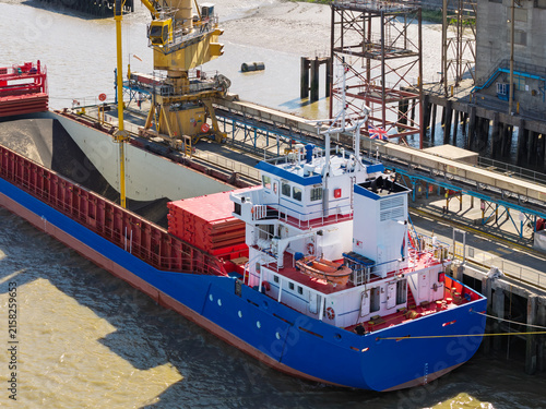 Large Cargo Ship Unloading Grain at a Busy Industrial River Port During the Day