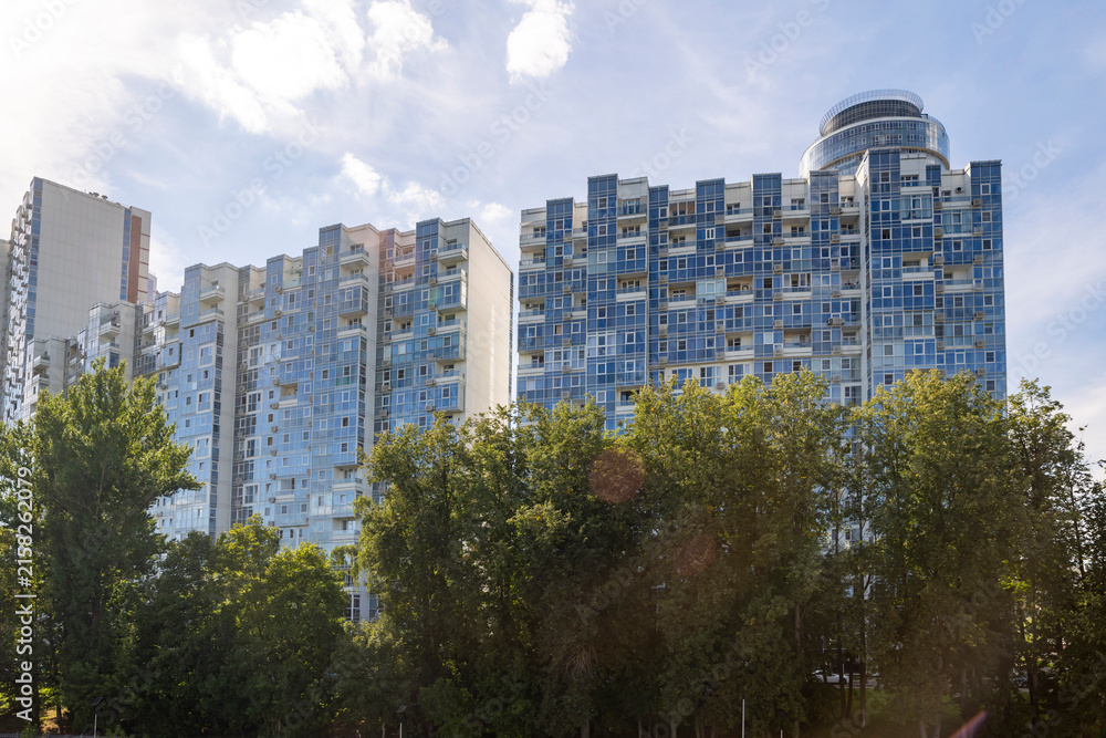 Fototapeta premium Moscow, Russia, August 5, 2026. High-rise blue glass residential buildings of the Mayak complex in Khimki behind green trees against a sunny sky with clouds.