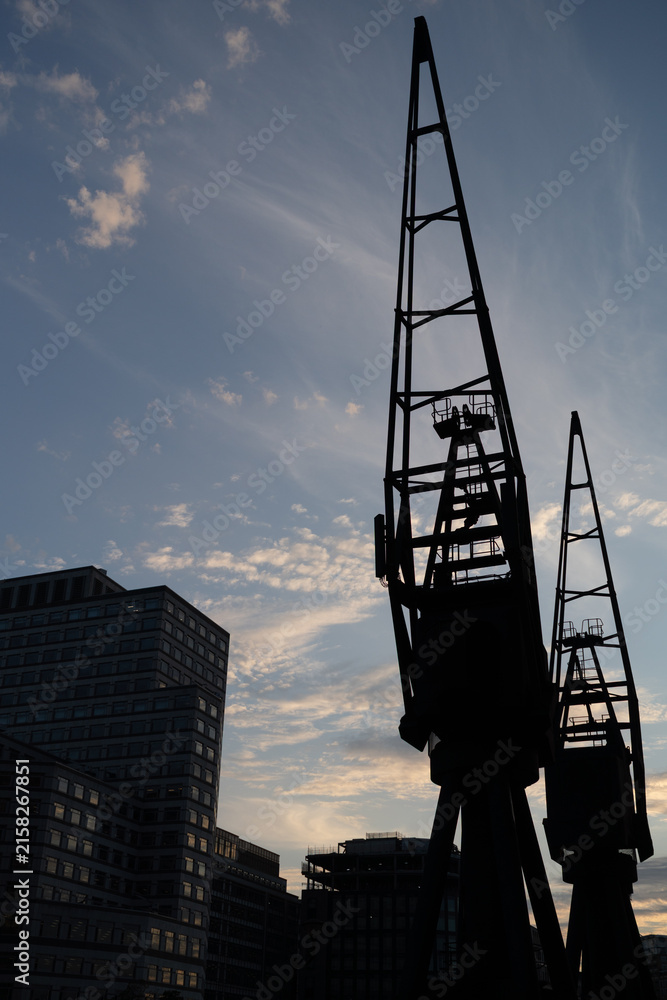 Fototapeta premium Silhouetted Industrial Cranes Against a Blue Evening Sky in Urban Setting